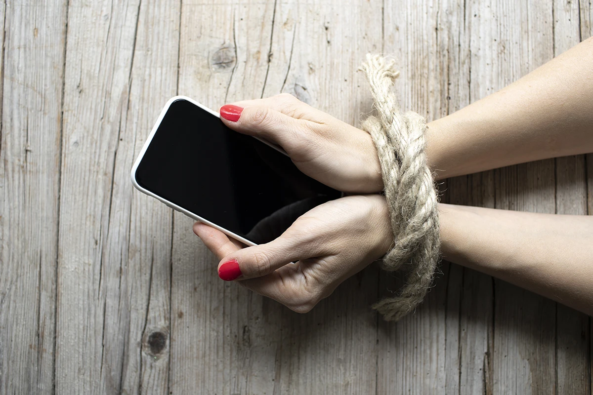 dłonie z komórką związane sznurkiem, symbolizujące uzależnienie od telefonów i komputera